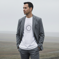Man wearing a gray blazer over a white t-shirt with a black design, standing in a misty landscape.