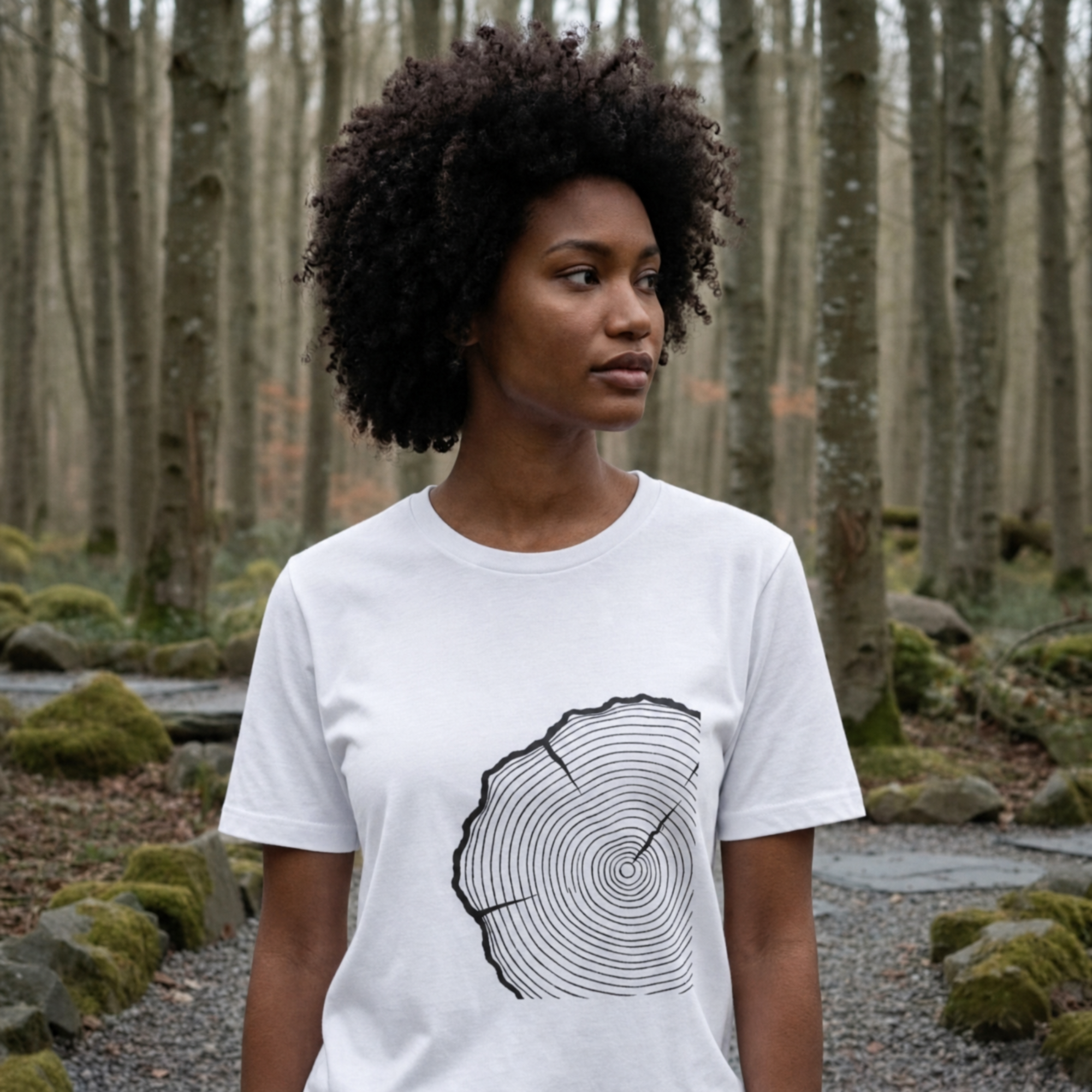 Woman wearing a white t-shirt with a tree ring design in a forest setting.