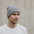 Man wearing a grey beanie with 'CREATED' text against a neutral background.