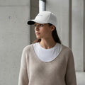 Woman wearing a white cap with 'CREATED' text and beige sweater against a neutral background.
