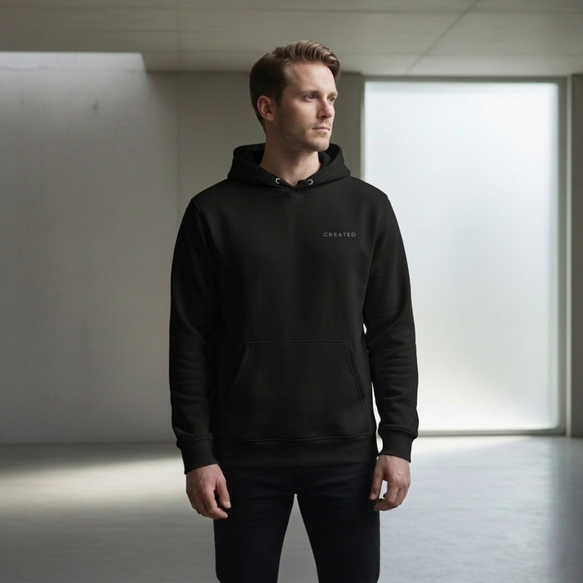 Man wearing a black hoodie with 'CREATED' logo in a neutral setting.