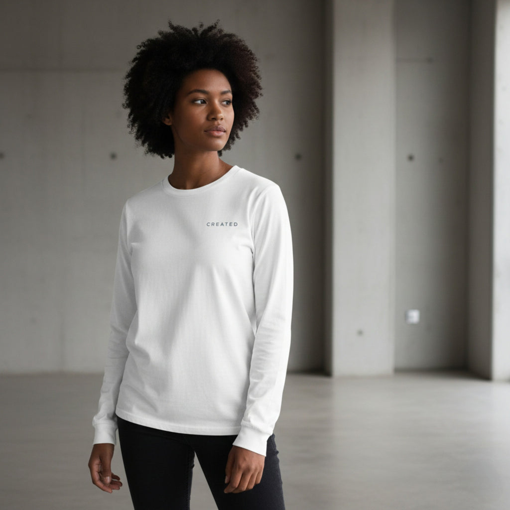 Woman wearing a white long-sleeve shirt with 'CREATED' text in a minimalistic setting.
