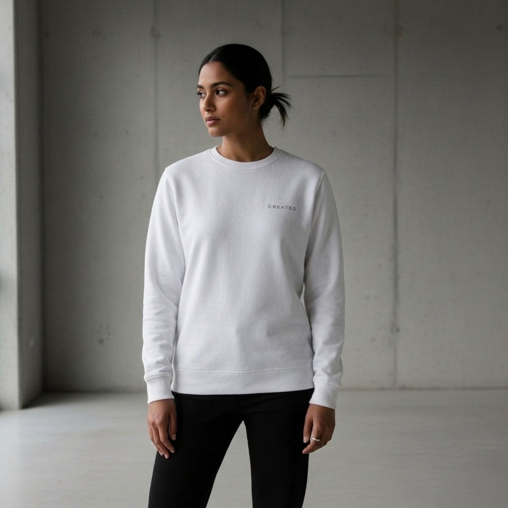 Woman wearing a white sweatshirt with a brand logo 'CREATED' in a minimalistic setting.