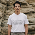 Man wearing a white t-shirt with a graphic design in front of a rocky background.